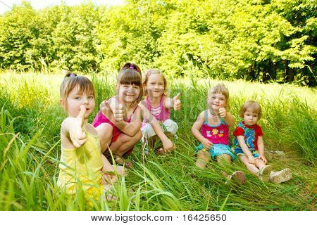 Group of five happy kids sitting in the grass