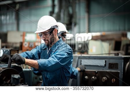 Men Industrial Engineer Wearing A White Helmet While Standing In A Heavy Industrial Factory Behind. 