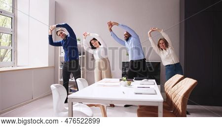 Happy Businesspeople Doing Stretching Exercise Behind Desk At Workplace