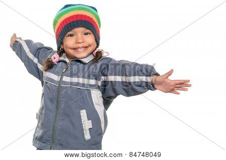 Happy mixed race little girl wearing a colorful beanie hat offering a hug with wide open arms isolated on white