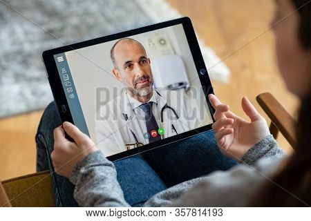 Back view of woman making video call with her doctor while staying at home. Close up of patient in video conferencing with general practitioner on digital tablet. Sick girl in online consultation.