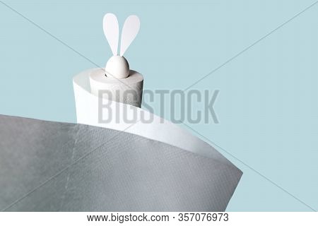 White Egg With Hare Ears In A Roll Of Toilet Paper. Hard Shadow On A Light Background. Concept On Ea