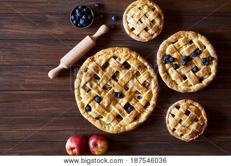 Homemade pastry apple pie pies bakery products on dark wooden kitchen table with raisins, blueberry and apples. Traditional dessert on Independence Day. Flat lay food background. Top view