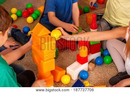 Children playing in kids cubes indoor. Lesson in primary school. Body part of girl and boy together play. Kindergarten kids sit on soft carpeton floor .