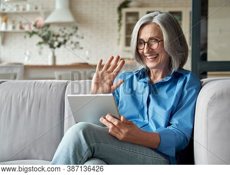 Happy 60s Older Mature Middle Aged Adult Woman Waving Hand Holding Digital Tablet Computer Video Con