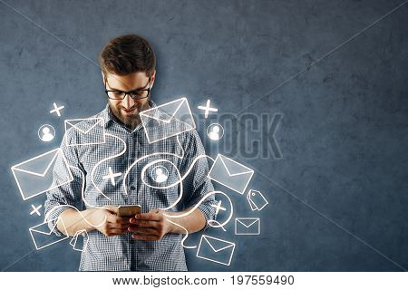 Cheerful young european man using smartphone with abstract email network on concrete wall background. Social media concept