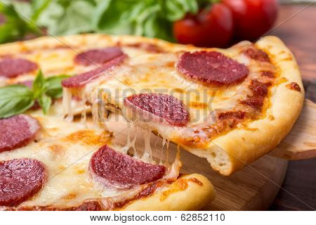 Slice of Pepperoni Pizza  being removed from whole pizza with tomatoes in background