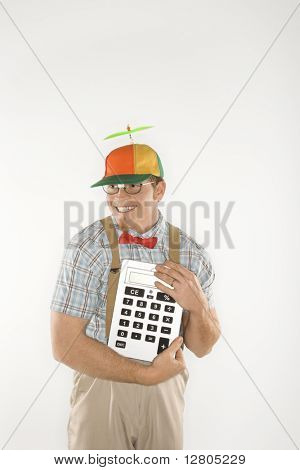 Caucasian young man dressed like nerd wearing beanie and smiling while holding large calculator.