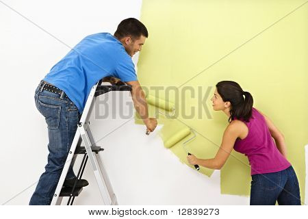 Attractive young adult couple painting interior wall of house.