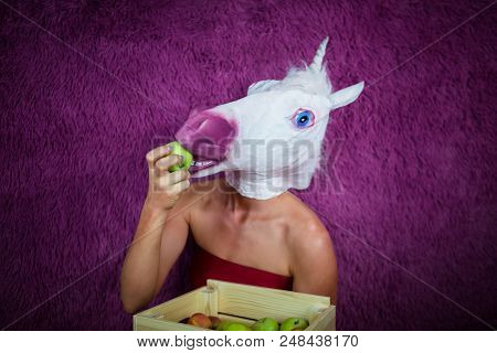 Freaky Young Woman In Comical Mask Stands On The Purple Background And Shows Box Of Fruits. Funny Gi