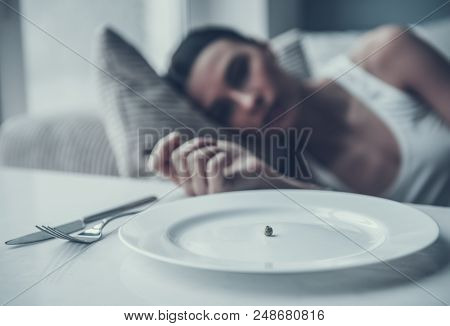 Young Woman Lying On Sofa Near Plate With Pea. Diet Concept. Weight Loss Problem. Starving Young Wom