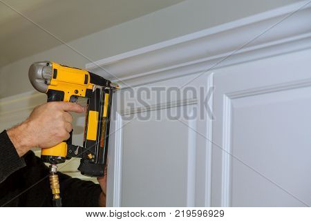 Wood working using brad nail air gun to Crown Moulding on white kitchen cabinets framing trim, with the all power tools