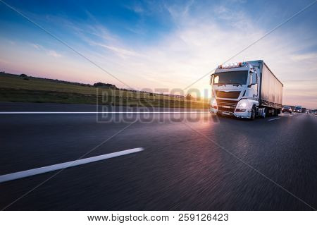 Loaded European truck on motorway in beautiful sunset light. On the road transportation and cargo.