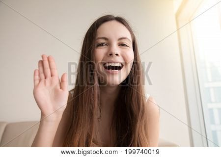 Smiling young woman waving with hand talking on camera, popular vlogger saying hello to followers communicating by webcam online or recording videoblog, happy teen girl making video call, head shot