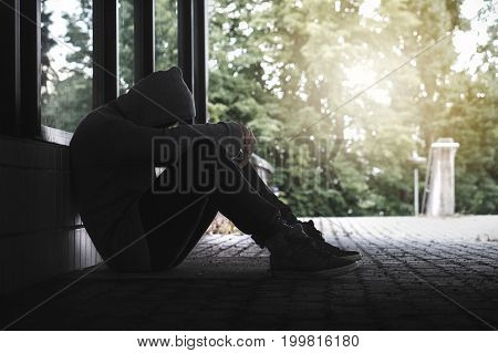 Depression, social isolation, loneliness, mental health and discrimination concept. Sad, lonely, depressed and unhappy man. Hooded person sitting in dark alley.