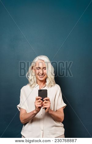 Image of happy mature old woman using mobile phone chatting. Looking aside.