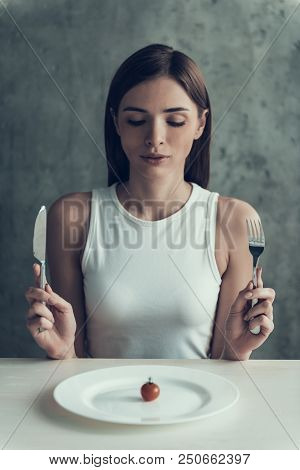 Woman Sitting On Chair And Eating Tomato On Plate. Diet Concept. Weight Loss Problem. Starving Young