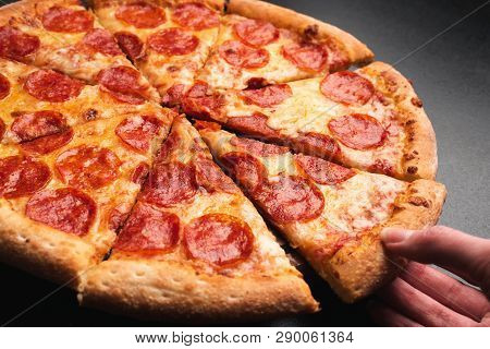 Taking Slice Of Pepperoni Pizza. Tasty Pepperoni Pizza On Black Background, Closeup View. Hand Takin