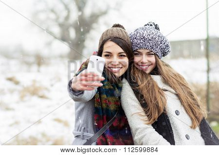 Two teenage girlfriends taking a selfie in winter