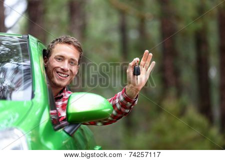 Car driver showing car keys and thumbs up happy. Young man holding car keys for new car. Rental cars or drivers licence concept with male driving in beautiful nature on road trip.