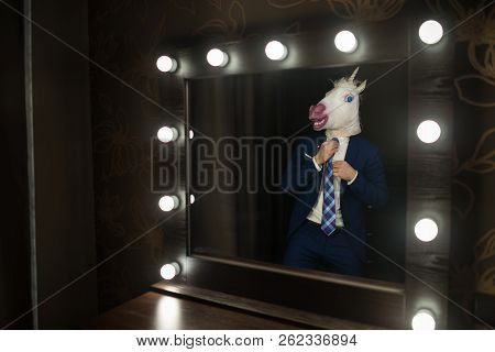 Glamour Guy In Elegant Suit And Comical Mask Looks At Himself In The Mirror In Dressing Room. Freaky