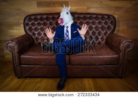 Funny Unicorn In Elegant Suit Siting On Sofa Like A Boss And Showing Do Not Bother Me Gesture. Portr