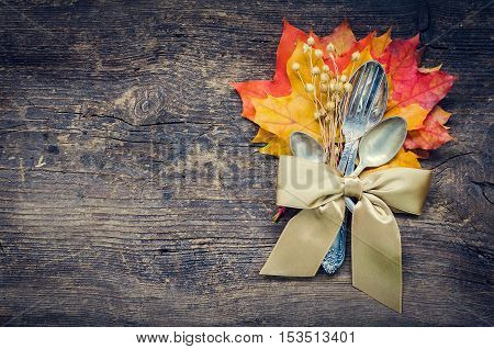 Thanksgiving autumn place setting with cutlery and arrangement of fall leaves and ribbon on wooden background with place for text. Thanksgiving holidays background concept. Copy space. Top view.