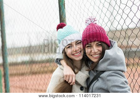 Two happy teenage girls in beanies hugging