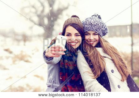 Two happy teenage girlfriends taking a selfie on snowy winter day