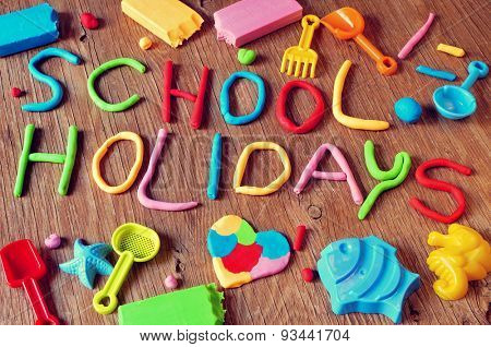 the text school holidays made from modelling clay of different colors and some beach toys such as toy shovels and sand moulds, on a rustic wooden surface