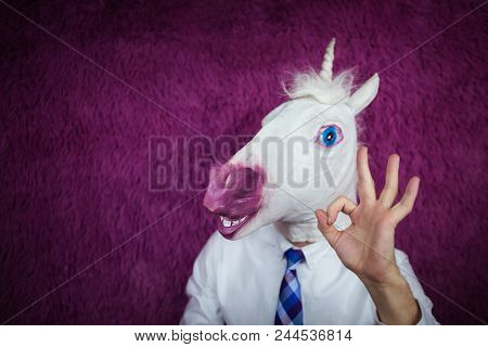 Freaky Young Man In Comical Mask Stands On The Purple Background. Portrait Of Unusual Manager. Funny