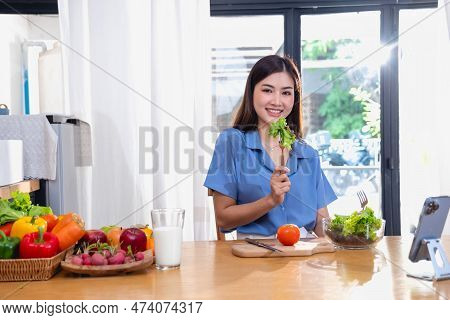 A Young Woman With A Beautiful Face In A Blue Shirt With Long Hair Eating Fruit Sitting Inside The K