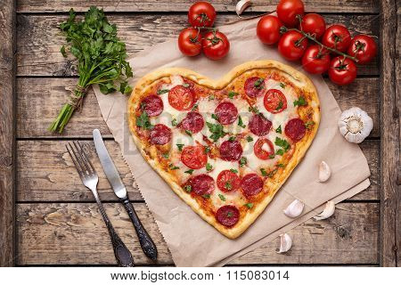 Heart shaped pizza for Valentines day with pepperoni, mozzarella, tomatoes, parsley and garlic on vi