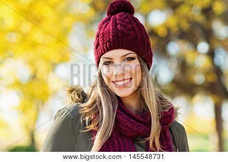 Closeup portrait of gorgeous young blonde Caucasian woman in knitted beanie and scarf in autumn in park. Young woman head shot, natural light, retouched, vibrant colors.