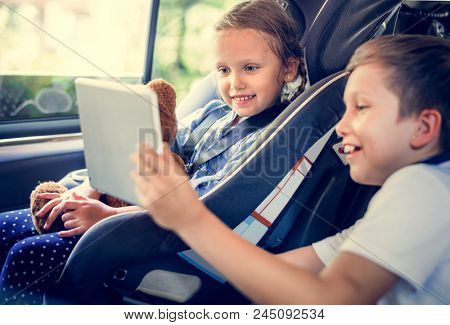 Sister and brother playing with digital devices in the car