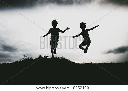 Silhouettes of kids jumping from a sand cliff at the beach