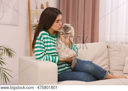 Woman Kissing Her Cute Cat On Comfortable Sofa At Home