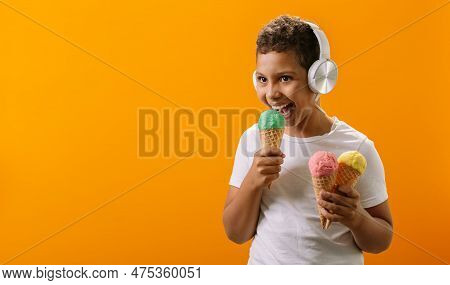 A Black Boy Holds Portions Of Ice Cream In His Hands. The Child Enjoys Music And Different Flavors O