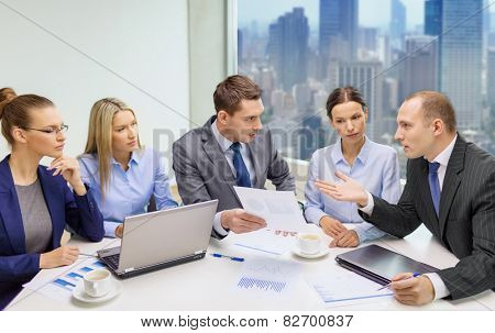 business, technology and people concept - business team with laptop computers, documents and coffee having discussion in office