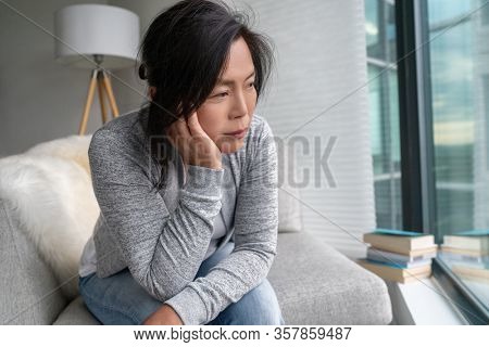 Sad Asian mature woman lonely at home self isolation quarantine for COVID-19 Coronavirus social distancing prevention. Mental health, anxiety depressed thinking senior chinese lady.