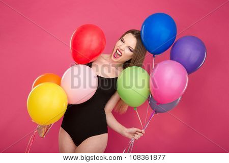 Crazy freaky bizarre screaming young woman in black leotard pozing with colorful balloons on pink background