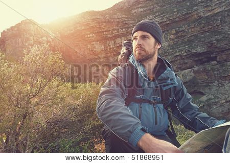 portrait of adventure man with map and extreme explorer gear on mountain with sunrise or sunset