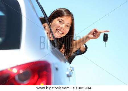 Woman driver holding car keys driving her new car. Beautiful multiracial young woman.