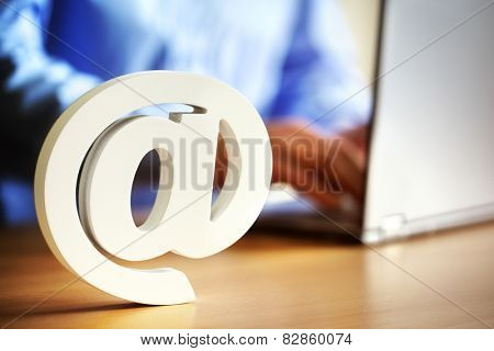 E-mail at symbol on an office desk with man on laptop computer