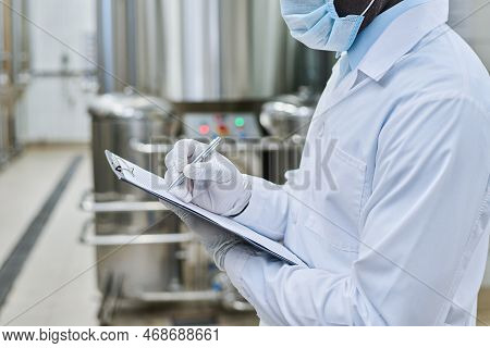 Close-up Of Engineer In Uniform And Protective Mask And Gloves Filling Document During His Work At C