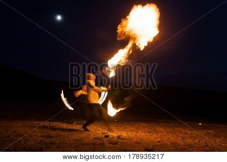 fire show, dancing with flame, male master fakir blowing fire, performance outdoors, flame control man dances with fire, draws a fiery figure in the dark, highly in mountains with a moon in a dark blue sky