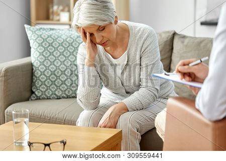 geriatric psychology, mental therapy and old age concept - sad unhappy senior woman patient and psychologist with clipboard taking notes at psychotherapy session