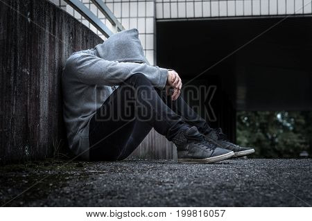 Depression, social isolation, loneliness, mental health and discrimination concept. Sad, lonely, depressed and unhappy man. Hooded person sitting in dark alley.