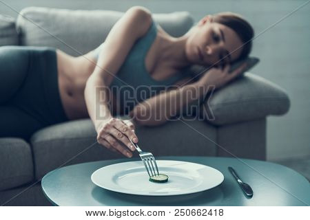 Young Woman Lying On Sofa And Eating One Pea. Diet Concept. Weight Loss Problem. Starving Young Woma