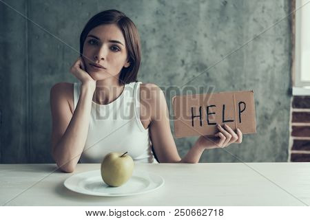 Young Woman With Sign Help And Eating One Apple. Diet Concept. Weight Loss Problem. Starving Young W